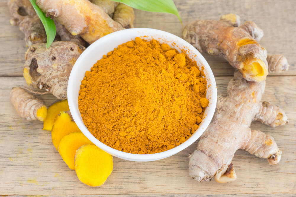 Bowl of turmeric powder with fresh turmeric roots, a top natural ingredient in skin whitening foods for brighter, glowing skin.