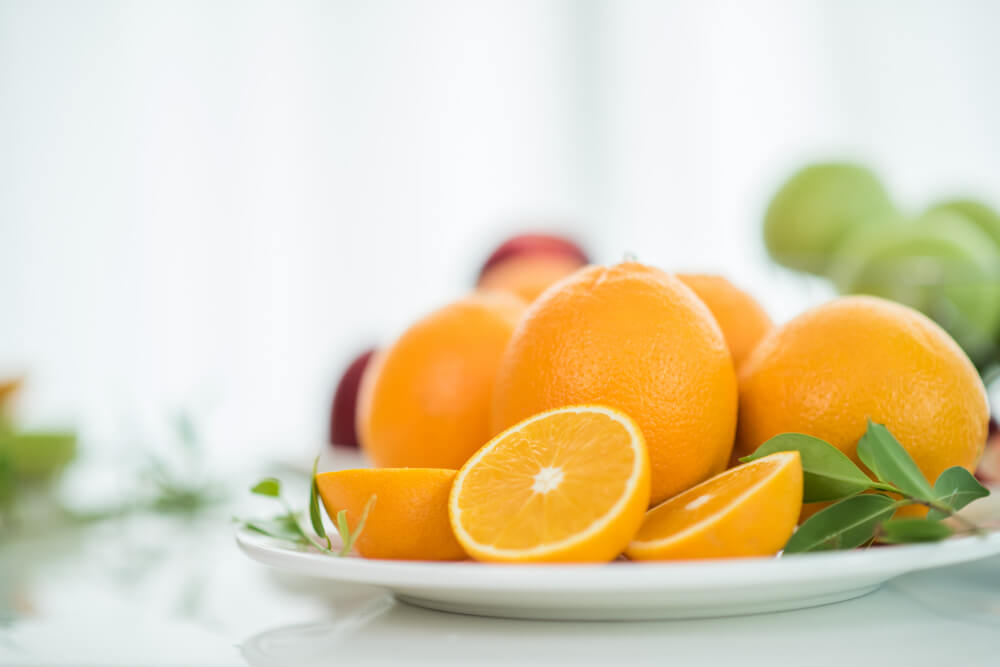 Fresh whole and sliced oranges on a plate, rich in vitamin C and known for their natural skin whitening benefits.